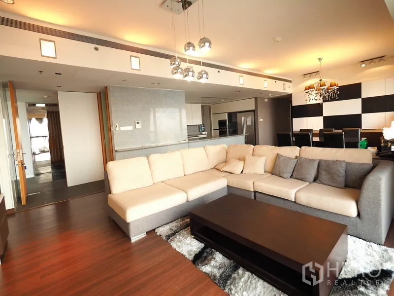 คอนโด ให้เช่าในSathon, Bangkok - มุมนั่งเล่นโซฟาตัวแอล โคมไฟแขวน และครัวเปิดเป็นฉากหลัง