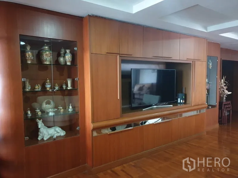 Condominium for rent in Khlong Toei, Bangkok - Living area feature wall with custom wood cabinetry, glass display shelves and flat-screen TV.