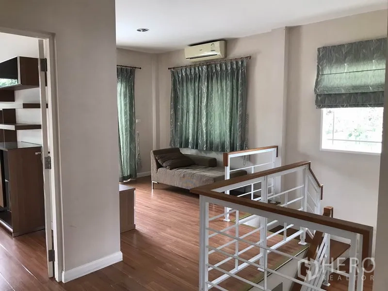 独立式住宅 出租在Khlong Sam Wa, Bangkok - 二楼走廊设日间床，通透窗户与白色楼梯扶手。
