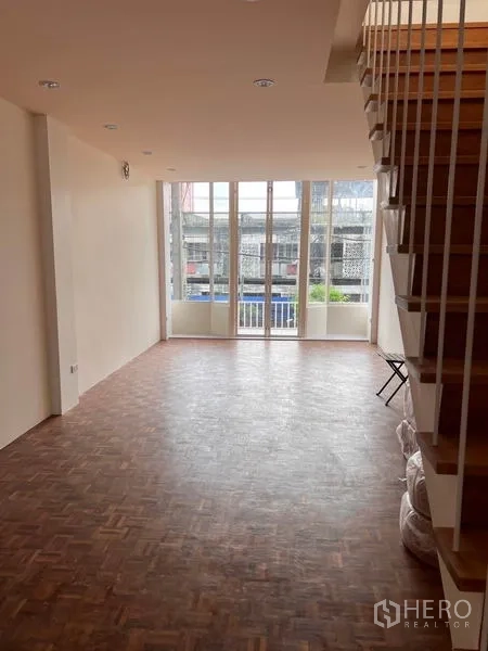Shophouse for rent or sale in Watthana, Bangkok - Bright room with parquet floor, full-height windows and staircase to upper level.