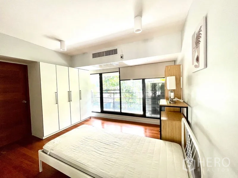 Townhouse for rent in Khlong Toei, Bangkok - Spacious bedroom with large wardrobe and balcony access via floor-to-ceiling glass.