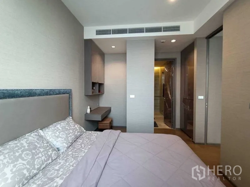 Condominium for rent or sale in Bang Rak, Bangkok - Bedroom with upholstered headboard, built-in desk and access to the ensuite bathroom.