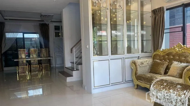 Detached House for rent or sale in Prawet, Bangkok - Bright living room with glass display cabinetry, ornate gold sofa and adjacent staircase.