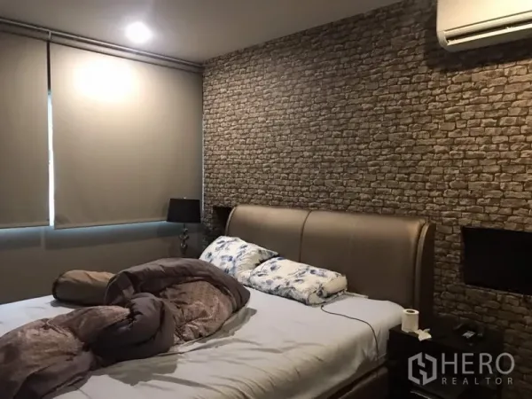 Townhouse for rent or sale in Suan Luang, Bangkok - Master bedroom with brick-pattern feature wall, upholstered bed, blackout blinds, and air conditioning.