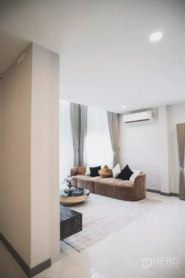 独立式住宅 出租在Bang Phli, Samut Prakan - 舒适休闲角，落地窗、米棕色沙发与空调、柔和窗帘。
