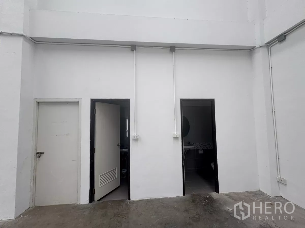 Factory for rent in Phra Samut Chedi, Samut Prakan - Ground-floor area with storage and restroom doors and exposed conduits.