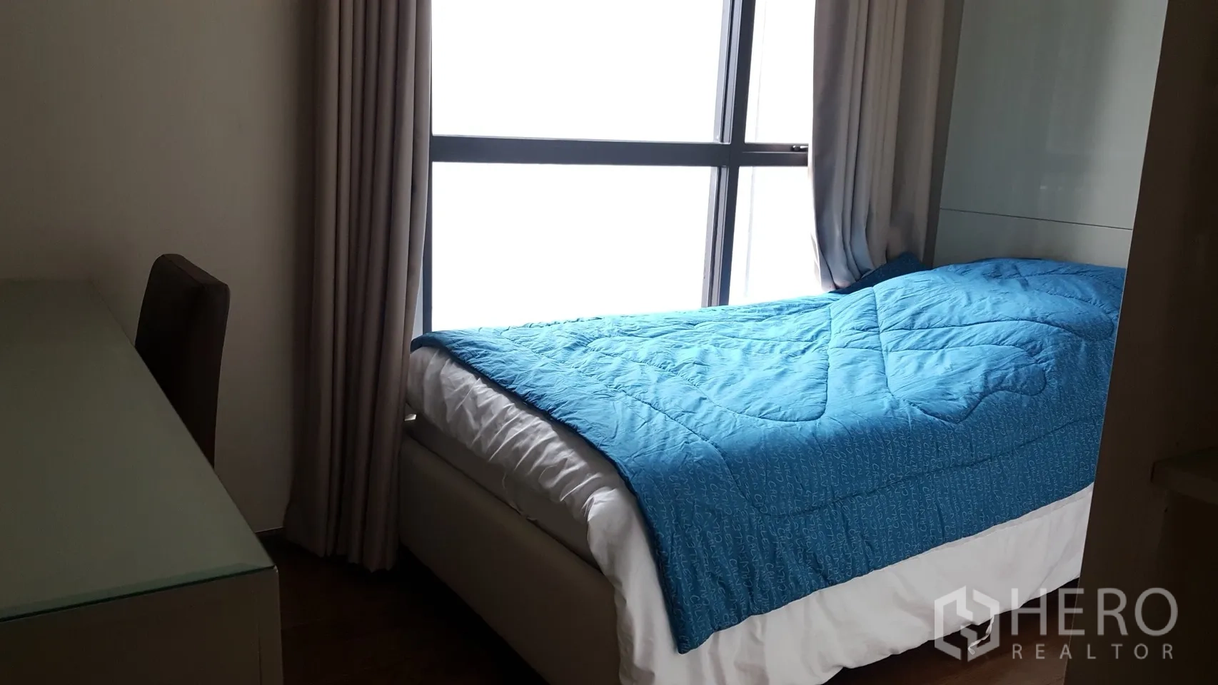 Condominium for rent or sale in Khlong Toei, Bangkok - Second bedroom with single bed, blue comforter, full-height window and a work desk.