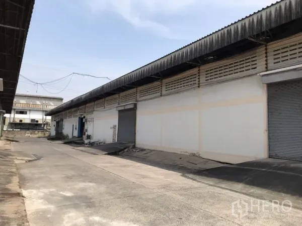 货栈 出租在Mueang Samut Prakan, Samut Prakan - 仓库外观，单层建筑，多个卷闸门，带装卸坡道与宽阔混凝土车道。
