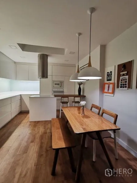 Townhouse for rent or sale in Yan Nawa, Bangkok - Minimal white kitchen with island cooktop, pendant lights and wood flooring.