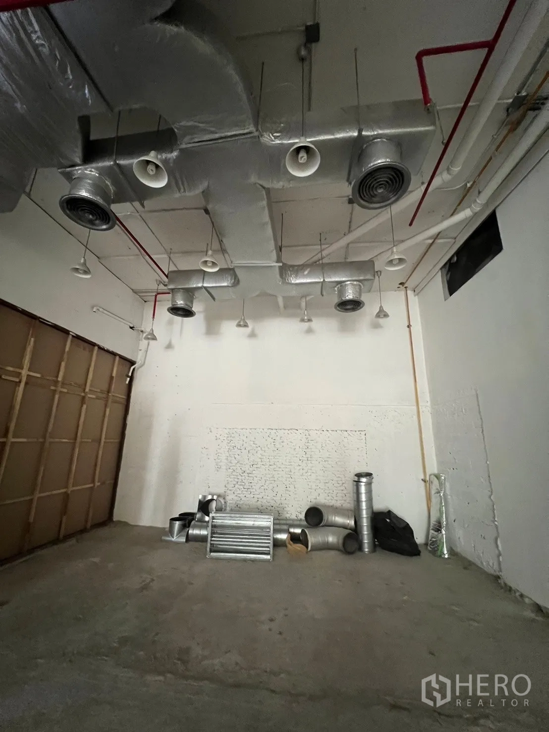 Retail Space for rent - Back area of the unit showing exposed HVAC ducts, sprinklers, and ventilation parts on the floor ready for installation.