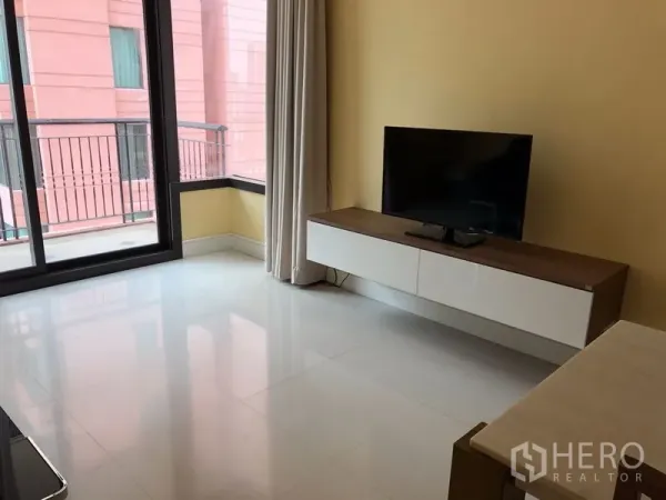 Condominium for rent or sale in Khlong Toei, Bangkok - Corner living area with TV console and floor-to-ceiling sliding doors opening to the balcony.
