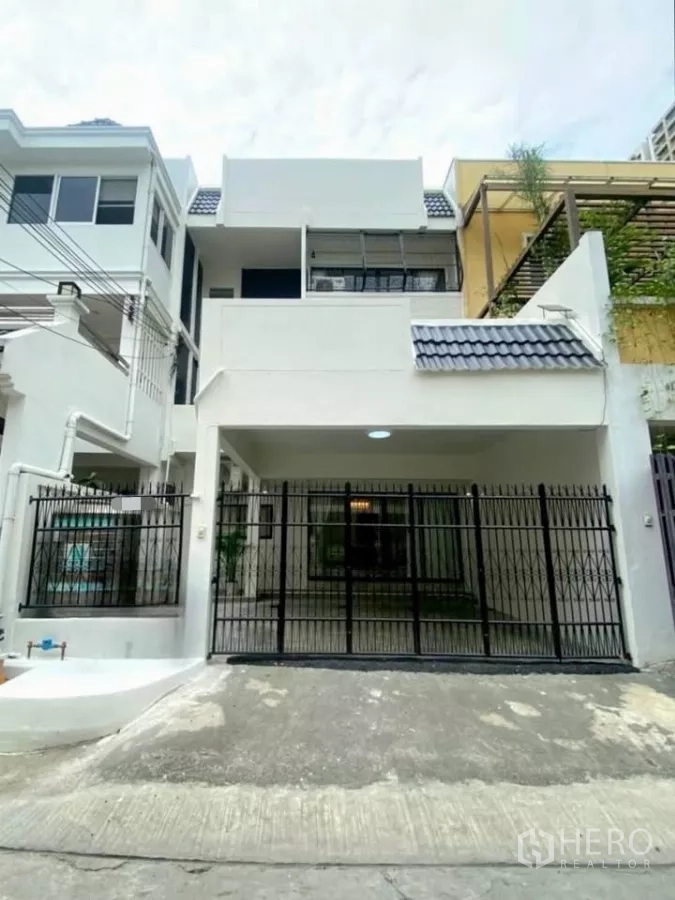 Townhouse for rent in Huai Khwang, Bangkok - Three-storey white townhouse facade with covered carport and black metal gate.