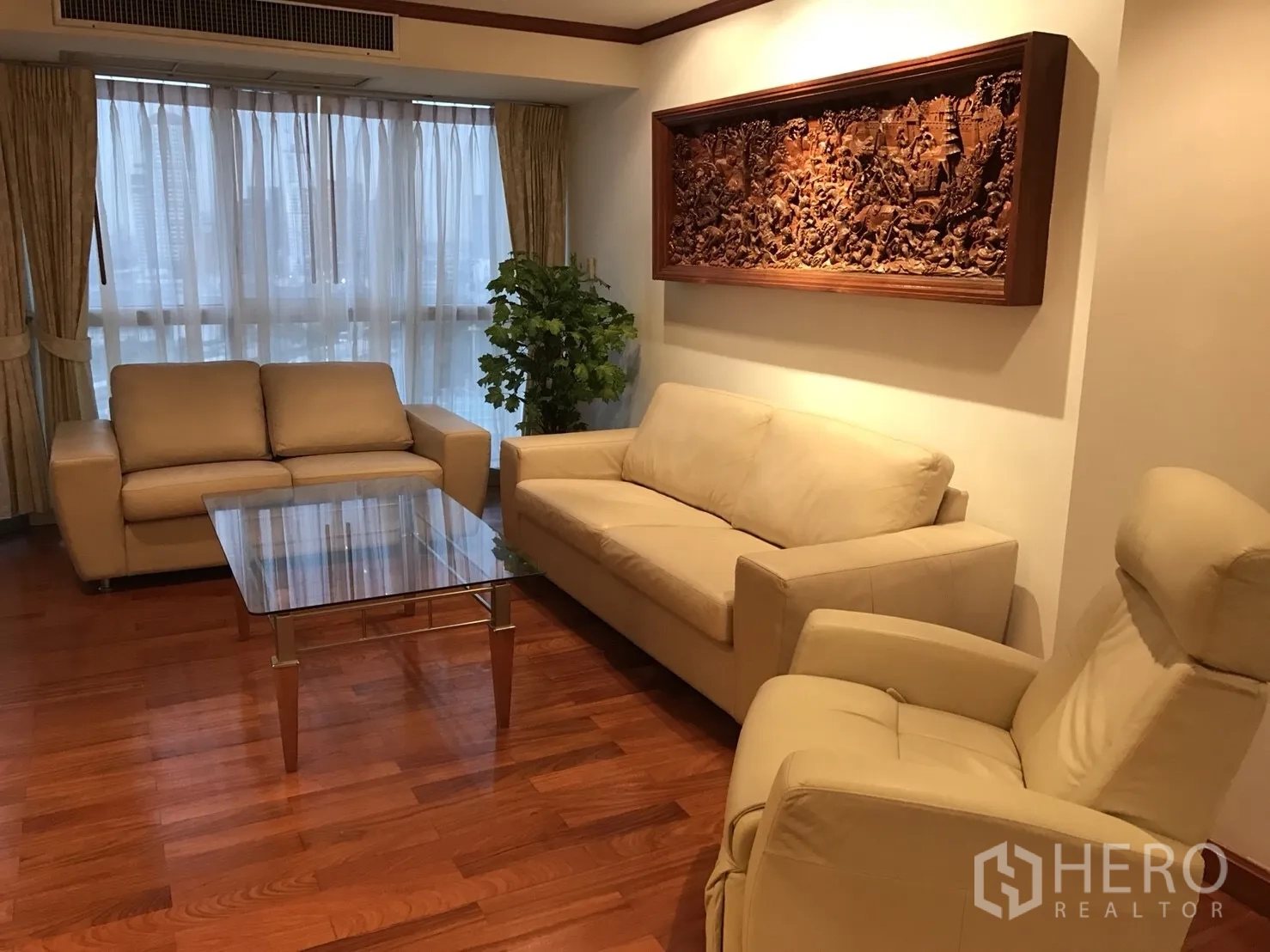 Condominium for rent in Khlong Toei, Bangkok - Living room with beige leather sofas, glass coffee table and picture window.