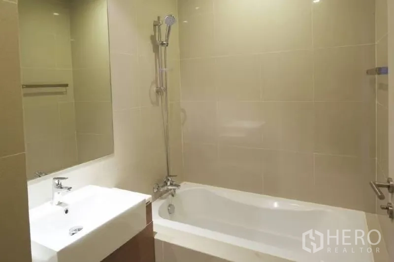 Condominium for rent in Bangkok - Modern bathroom with bathtub, wall shower and large mirror in neutral tiles.