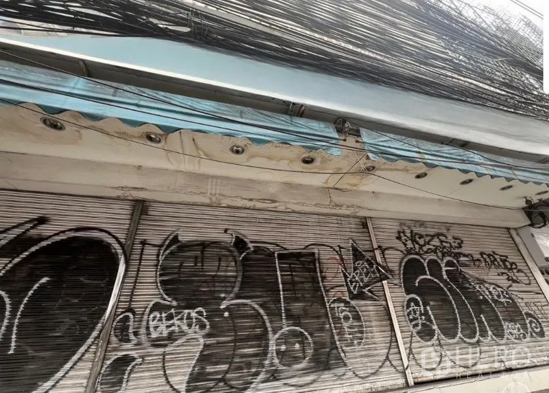 Shophouse for rent in Watthana, Bangkok - Streetfront shophouse with closed roller shutters covered in graffiti, awning and thick overhead cables.