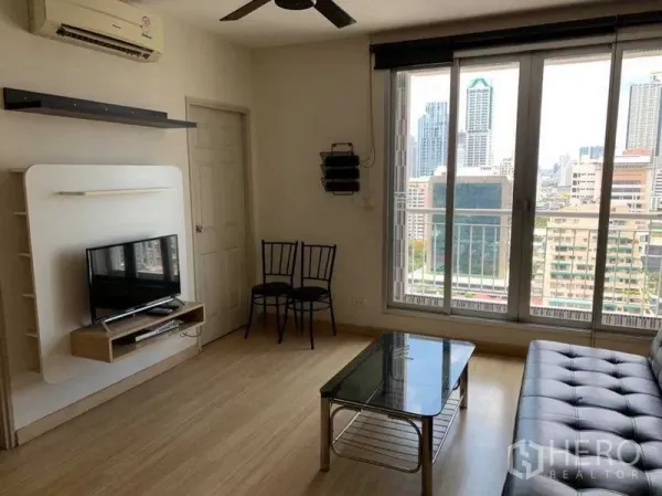 Condominium for rent in Bang Rak, Bangkok - Living area with balcony doors, wall-mounted TV shelf, glass coffee table and sofa.