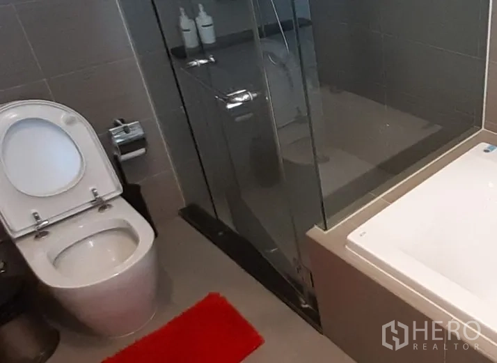 Condominium for rent in Khlong Toei, Bangkok - Main bathroom with glass shower and separate bathtub in gray tile.