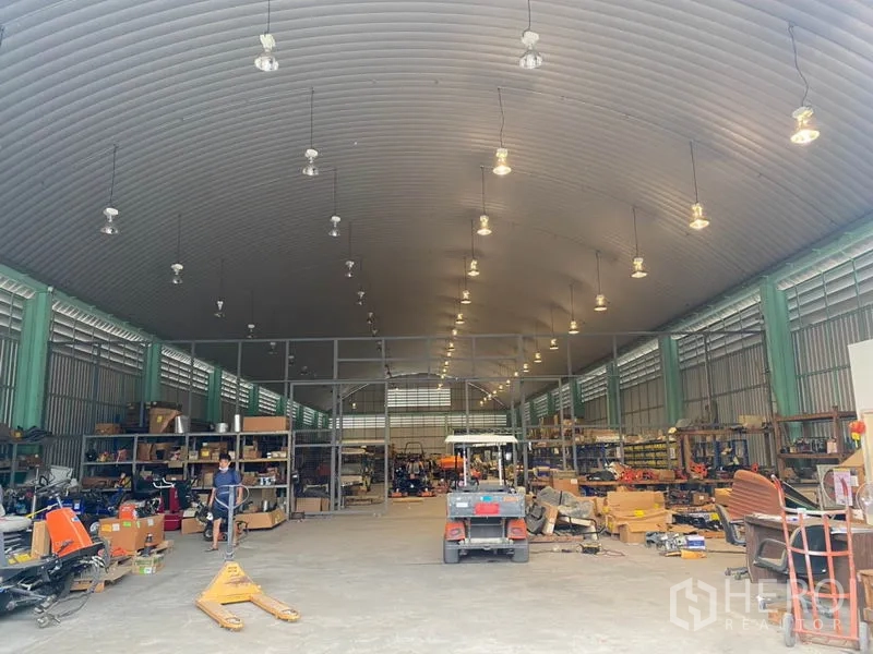 Warehouse for rent in Lak Si, Bangkok - Spacious warehouse interior with a high curved ceiling, multiple hanging lights, metal shelving and equipment storage area.