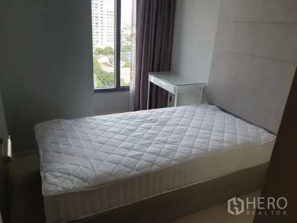 公寓 出租在Watthana, Bangkok - 次卧配床与转角窗、遮光窗帘和玻璃书桌，可眺望绿地与建筑。