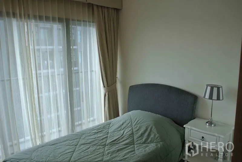 Condominium for rent in Khlong Toei, Bangkok - Cozy bedroom with floor-to-ceiling windows, sheer curtains and bedside table.
