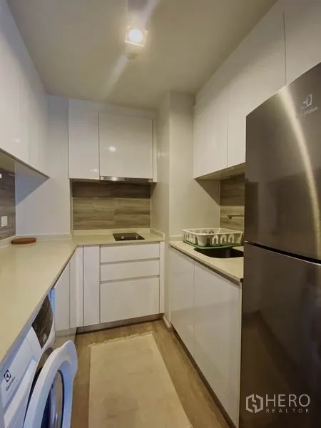 Condominium for rent in Pathum Wan, Bangkok - Compact modern kitchen with white cabinetry, electric hob, large fridge and washing machine.