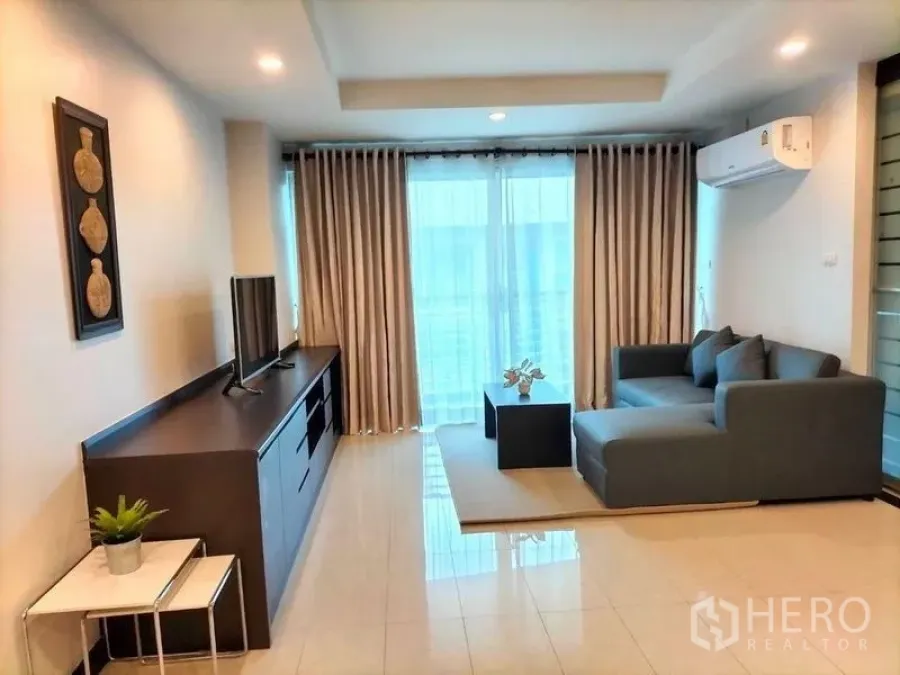คอนโด ให้เช่าในWatthana, Bangkok - ห้องนั่งเล่นสว่าง โซฟา L สีเทา ชั้นวางทีวี แอร์ และระเบียงพร้อมผ้าม่านสูงจรดเพดาน