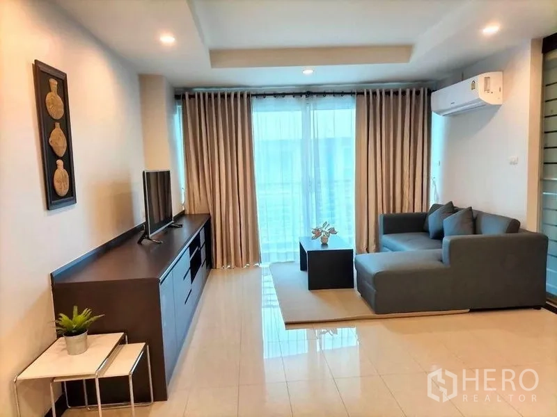 คอนโด ให้เช่าในWatthana, Bangkok - ห้องนั่งเล่นสว่าง โซฟา L สีเทา ชั้นวางทีวี แอร์ และระเบียงพร้อมผ้าม่านสูงจรดเพดาน