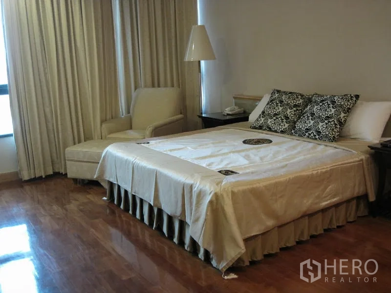 คอนโด ให้เช่าในPathum Wan, Bangkok - ห้องนอนพื้นไม้พร้อมเตียงคิง เก้าอี้เอน โต๊ะข้าง และผ้าม่านทึบเต็มความสูง