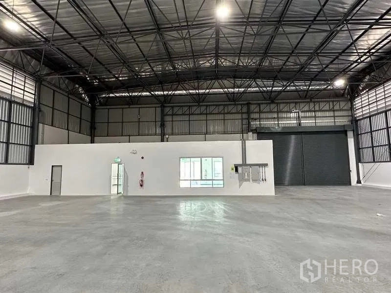 Factory for rent in Bang Sao Thong, Samut Prakan - Spacious warehouse interior featuring a high steel truss roof, polished concrete floor and a roller shutter.