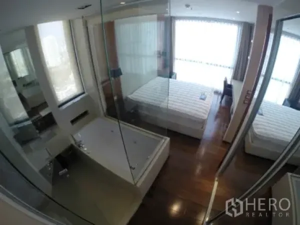 Condominium for rent in Khlong Toei, Bangkok - Master bedroom with floor-to-ceiling windows, hardwood floors, and a glass-walled bathtub suite.