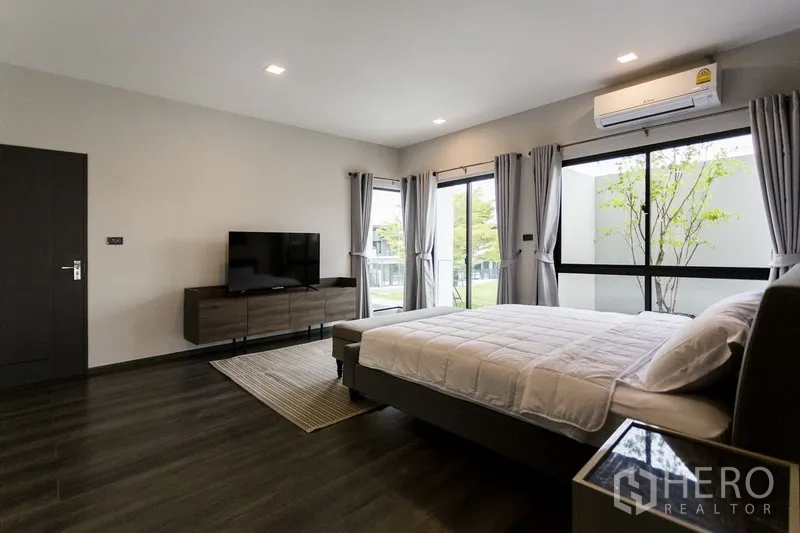 Townhouse for rent in Samut Prakan - Master bedroom alternate view showing TV console, corner windows and air-conditioning.
