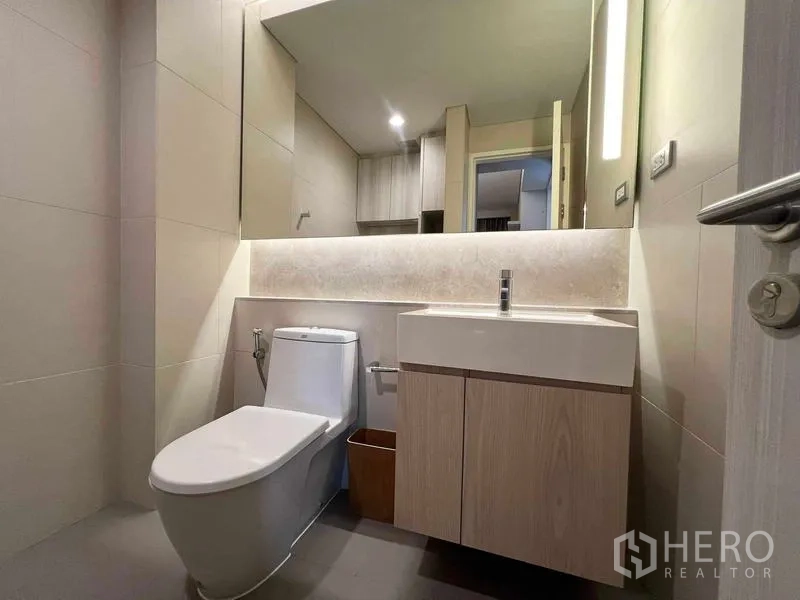 Condominium for rent or sale - Modern bathroom with vanity cabinet, large mirror, and toilet in neutral tiles.
