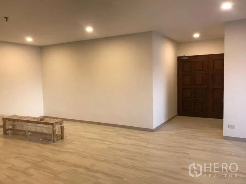 公寓 出售在Watthana, Bangkok - 宽敞客厅，浅色木地板、筒灯与实木入户门。