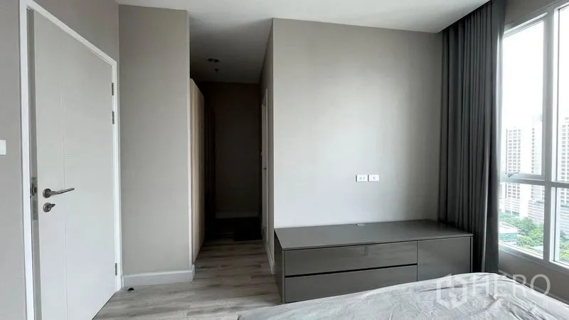 Condominium for sale in Sathon, Bangkok - Minimal bedroom corner with built-in dresser, white doors and a floor-to-ceiling window.