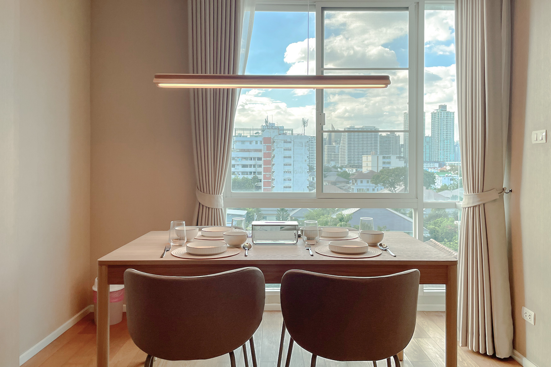 คอนโด ให้เช่าในWatthana, Bangkok - โต๊ะรับประทานอาหารสำหรับสี่ที่ริมหน้าต่าง มองเห็นสกายไลน์กรุงเทพฯ พร้อมโคมไฟแขวน