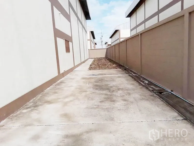 Factory for sale in Pathum Thani - Rear access driveway beside the warehouse with concrete pavement.