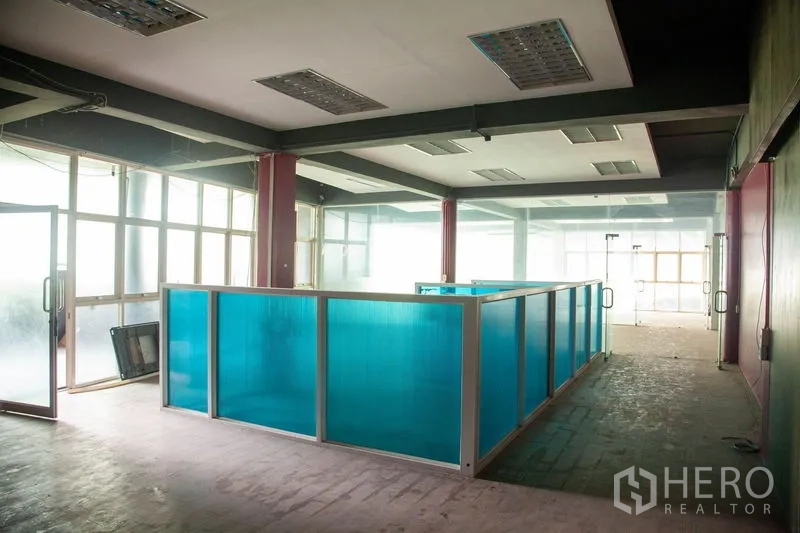 Warehouse for rent in Prawet, Bangkok - Open-plan work area with blue partitioned bays, fluorescent lighting and frosted windows inside a Prawet warehouse.