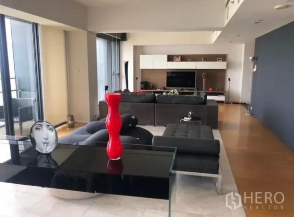 Condominium for rent in Sathon, Bangkok - Spacious modern living room with black sectional sofa, TV wall and floor-to-ceiling windows