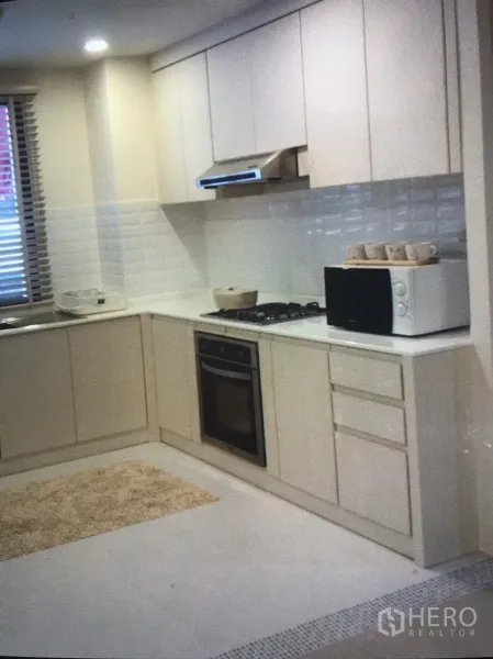 Condominium for rent in Bang Rak, Bangkok - Light L-shaped kitchen with white cabinets, gas hob, built-in oven, range hood and microwave.