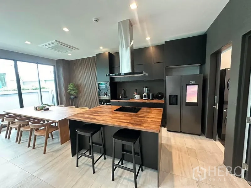 Detached House for rent in Saphan Sung, Bangkok - Modern kitchen with wood-topped island, dark cabinets and built-in appliances.