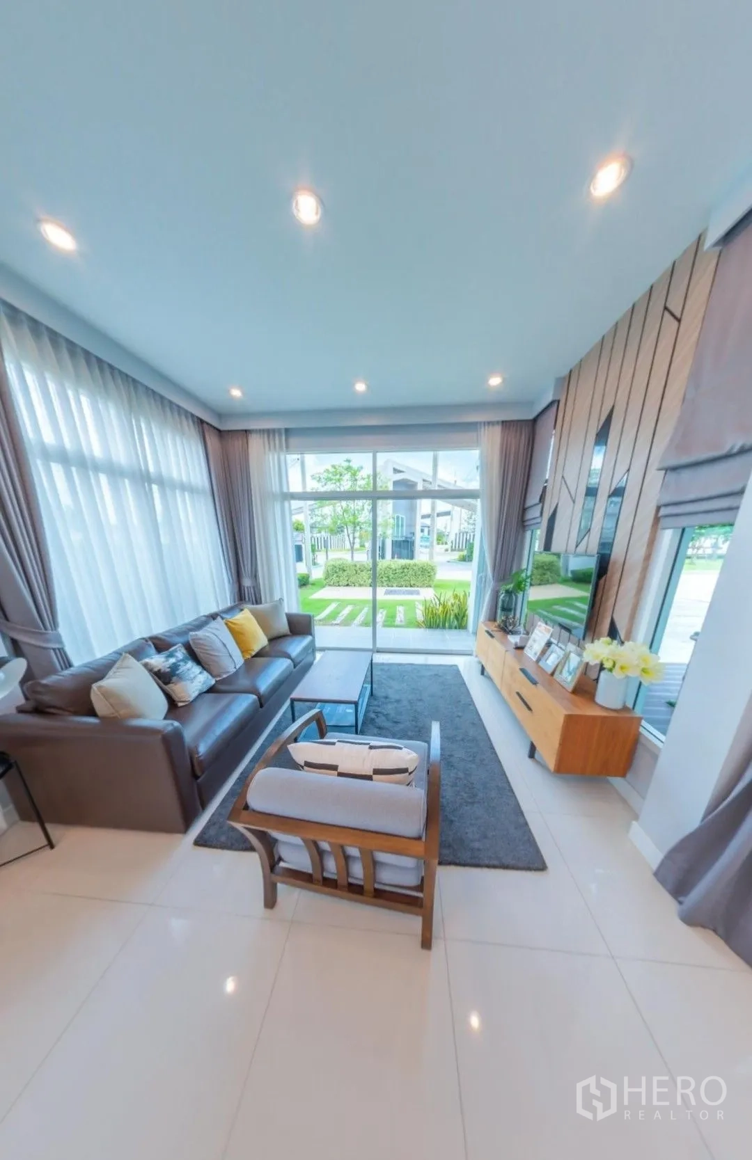Detached House for rent in Lam Luk Ka, Pathum Thani - Modern living room with large windows, sofa set, TV console, and garden view.