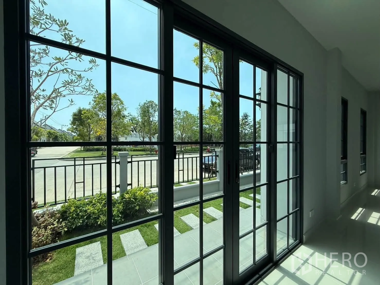 Detached House for rent in Bang Phli, Samut Prakan - Ground-floor view through black-framed sliding doors to a small garden and street.