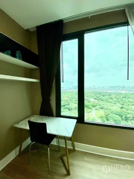 Condominium for rent in Bangkok - Compact study nook with shelves and marble desk beside a floor-to-ceiling window overlooking a green park.