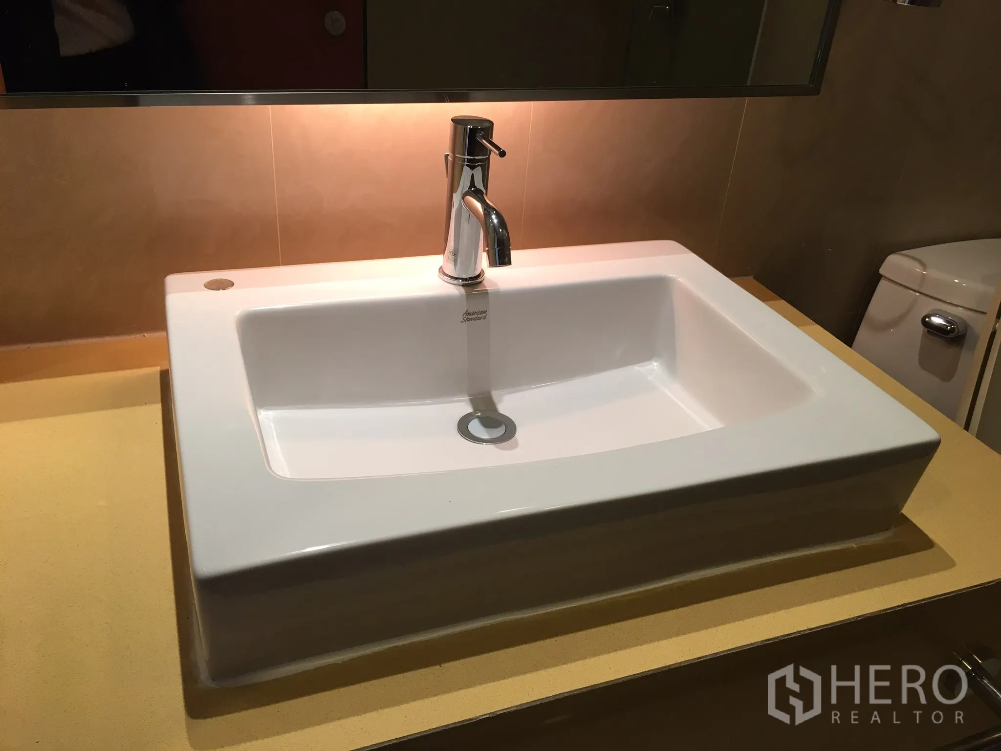 Condominium for rent in Khlong Toei, Bangkok - Modern bathroom with rectangular basin on a yellow countertop beside the toilet.