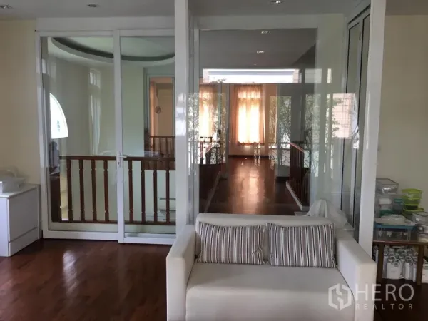 联排别墅 出售在Huai Khwang, Bangkok - 走廊与休息区由落地玻璃门分隔，木质楼梯扶手。
