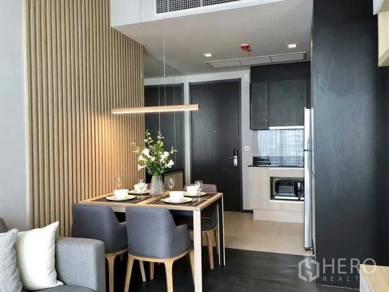 公寓 出租在Watthana, Bangkok - 现代小厨房带嵌入式柜体与微波炉，餐桌下方为线性吊灯照明。