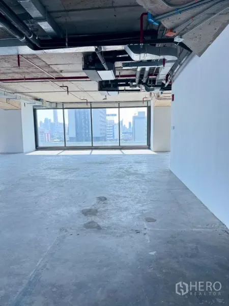 Office Space for rent in Din Daeng, Bangkok - Open-plan shell office with exposed ceiling ducts and a full-height window overlooking the Bangkok skyline.