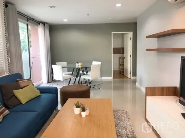 Condominium for rent or sale in Khlong Toei, Bangkok - Open-plan lounge and dining area with wall shelves and access to a side balcony.