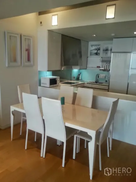 Condominium for rent or sale in Sathon, Bangkok - Dining table for six beside compact kitchen with glossy cabinets and accent lighting.