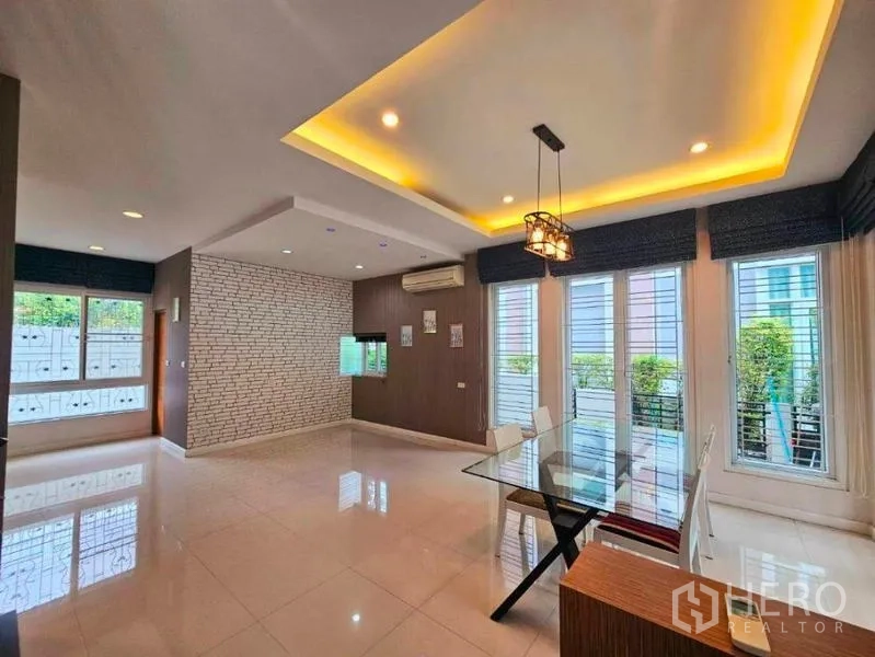 Detached House for rent in Chatuchak, Bangkok - Dining area with tray ceiling lighting, glass table and tall windows opening to greenery.